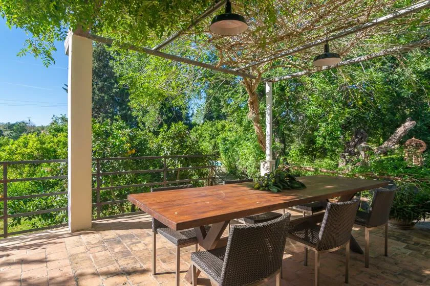 Una zona de comedor al aire libre con una mesa de madera bajo una pérgola frondosa.