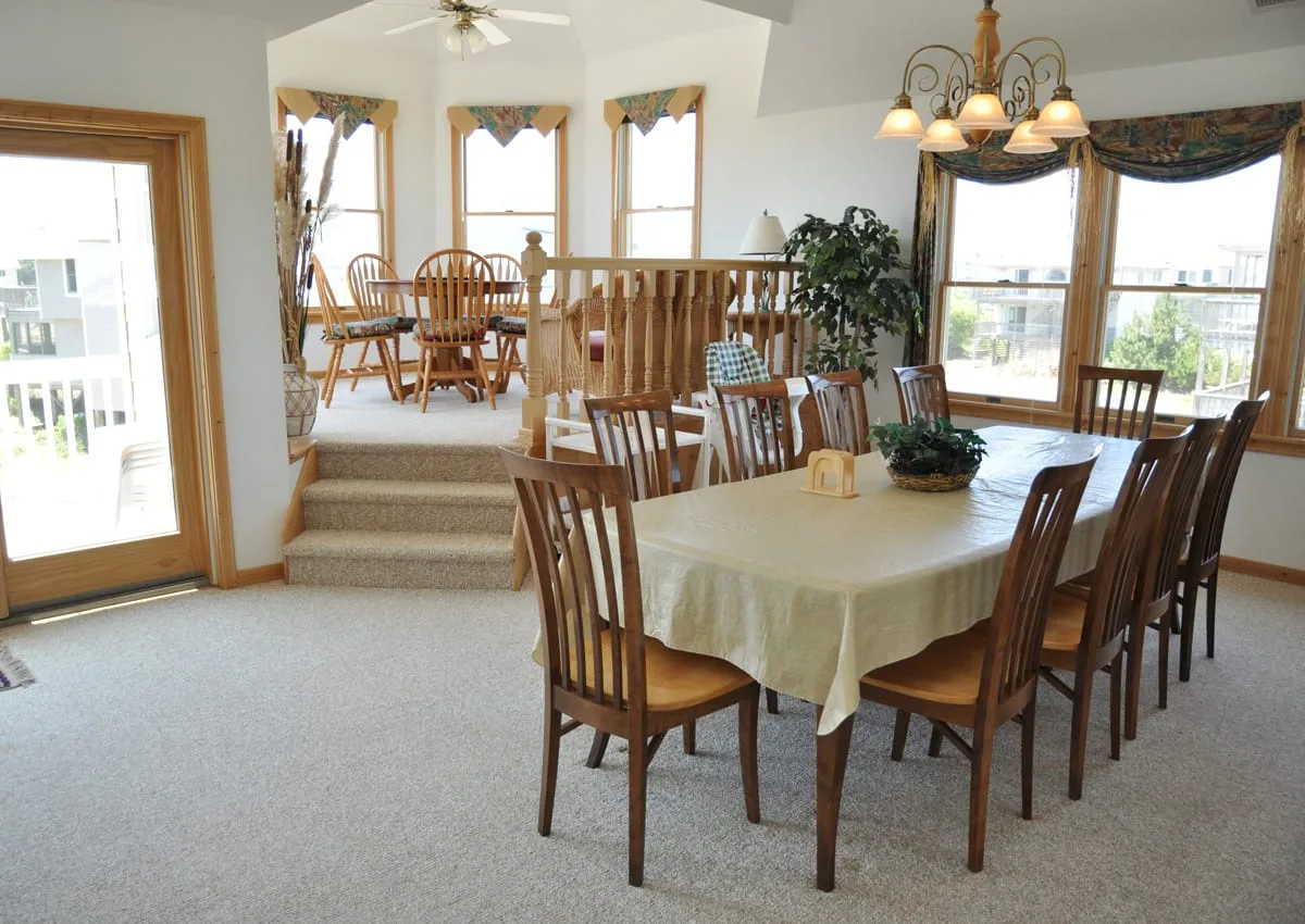 Comedor con una mesa grande y asientos de madera junto a ventanas luminosas.