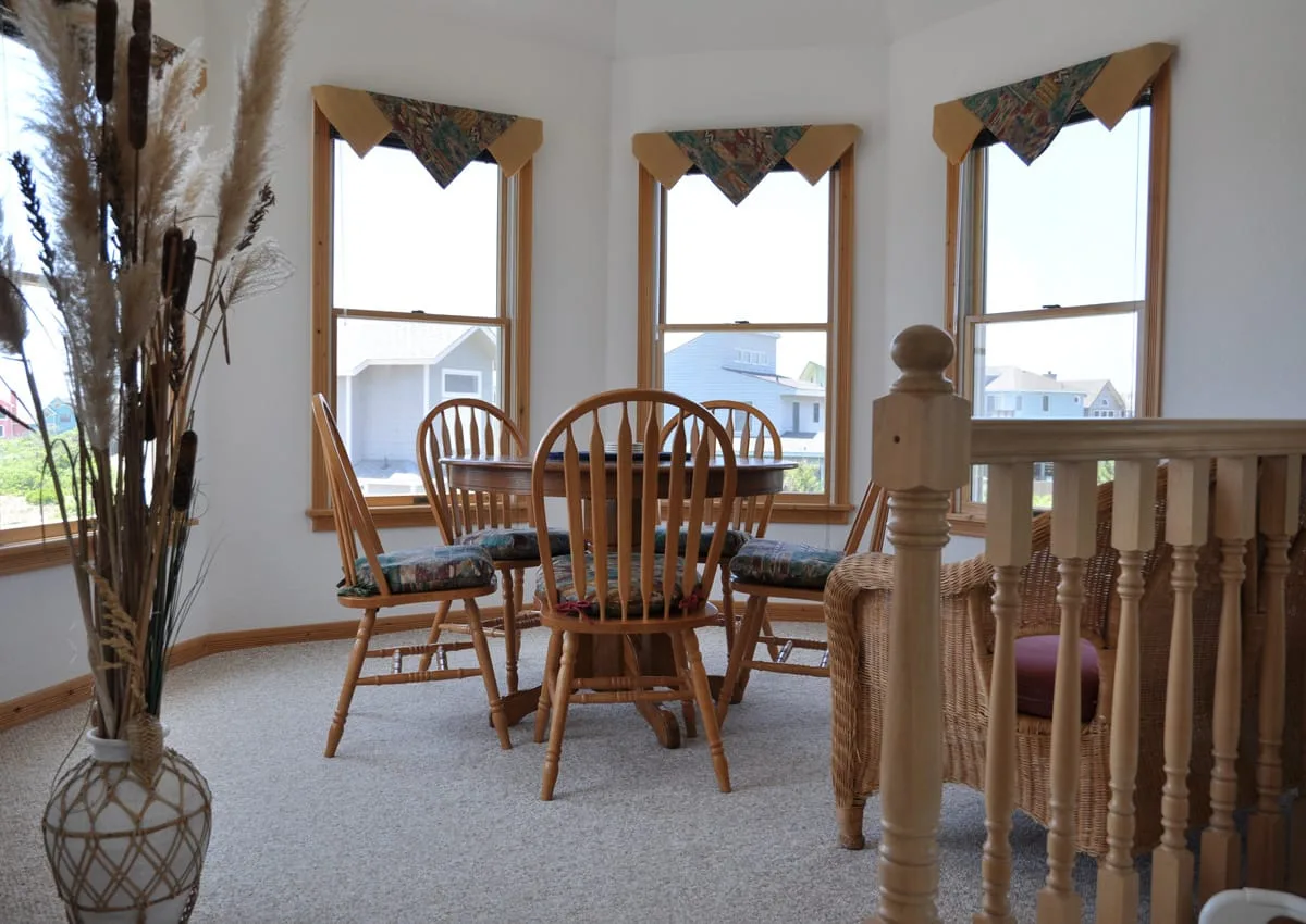 Un comedor con asientos de madera y ventanas con vista a casas vecinas.