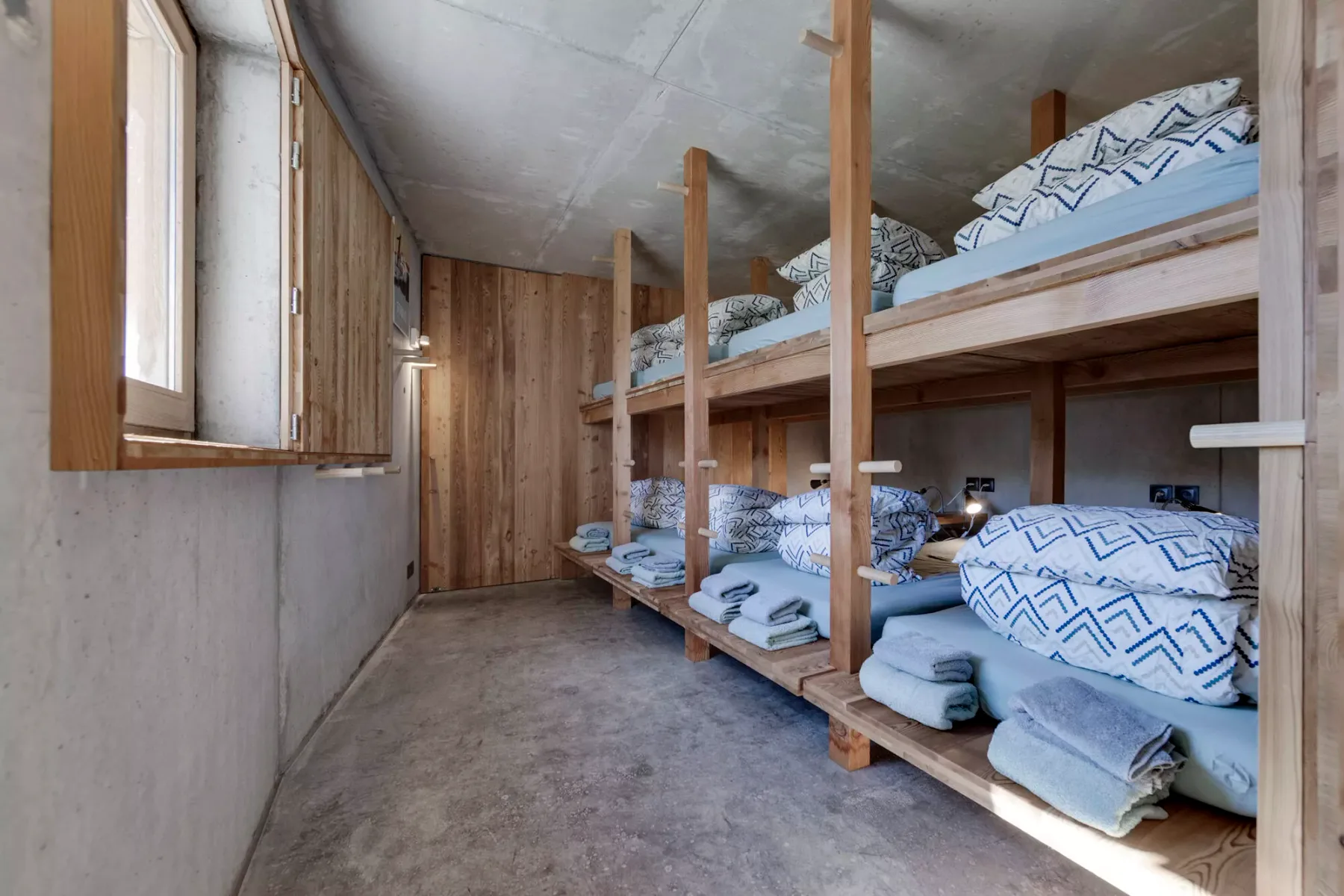 Un dormitorio con literas de madera, ropa de cama azul y una ventana abierta.