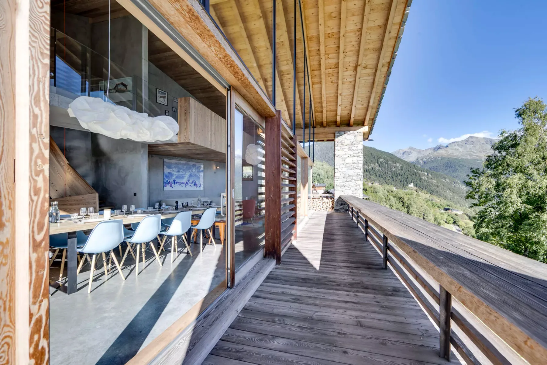 A wooden deck runs beside a glass-walled dining area, overlooking a mountain landscape.