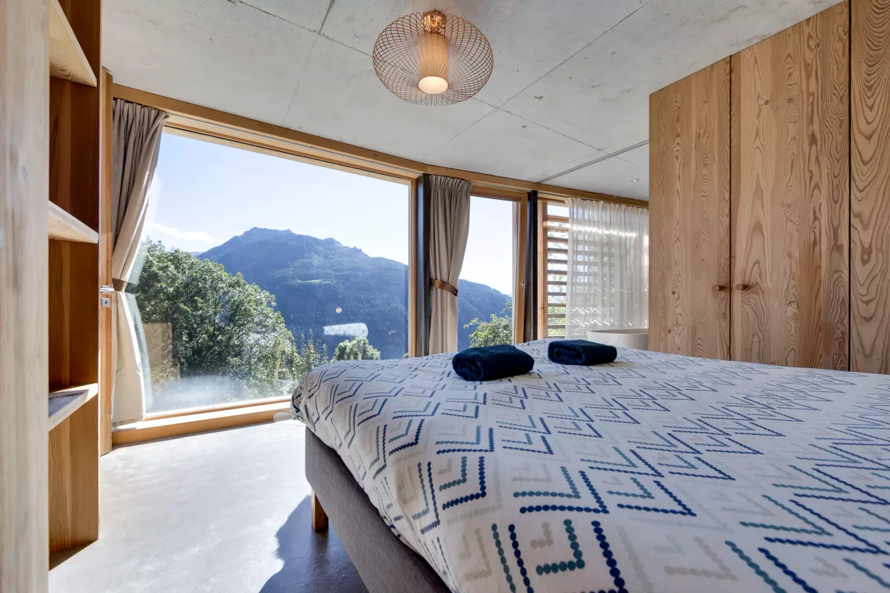Un dormitorio con ropa de cama estampada, armarios de madera y una gran ventana con vistas a las montañas.
