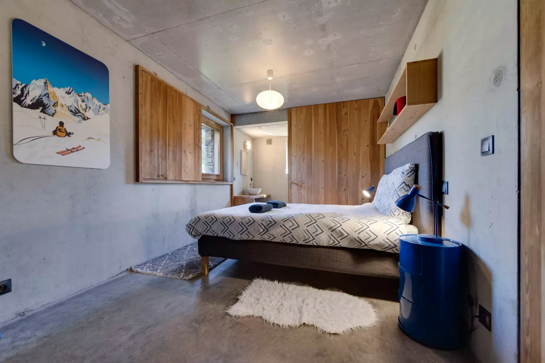 Un dormitorio con una cama doble, una pared revestida de madera y pequeñas alfombras en el suelo.