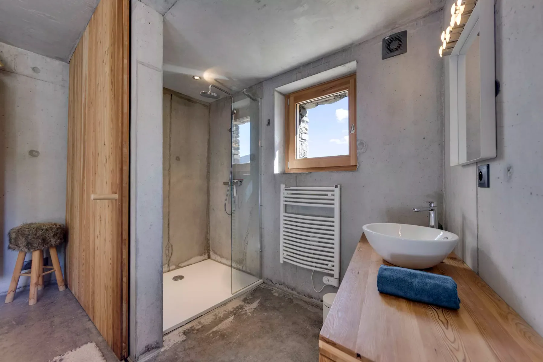 Un baño con ducha de cristal, ventana y mueble de madera.