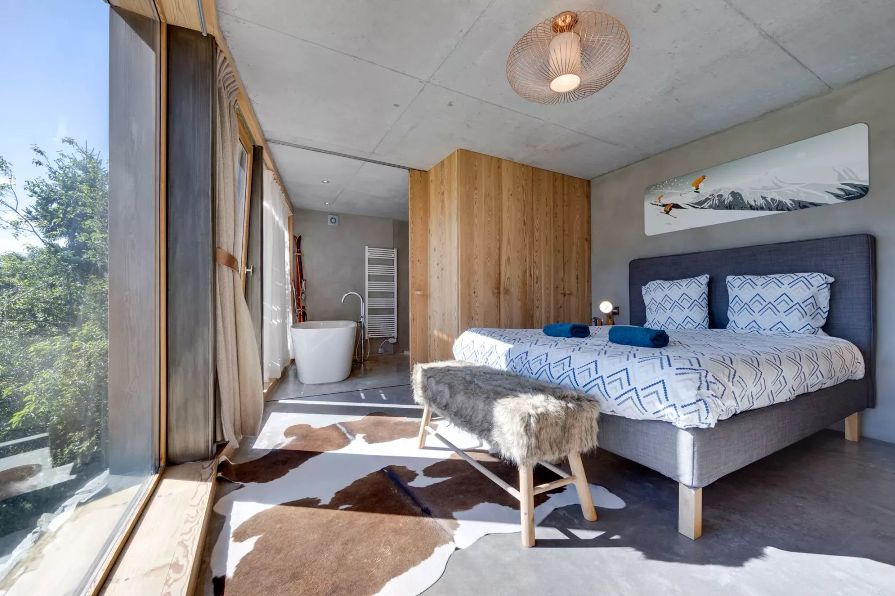 Un dormitorio con una cama estampada, un tabique revestido de madera y una bañera exenta.