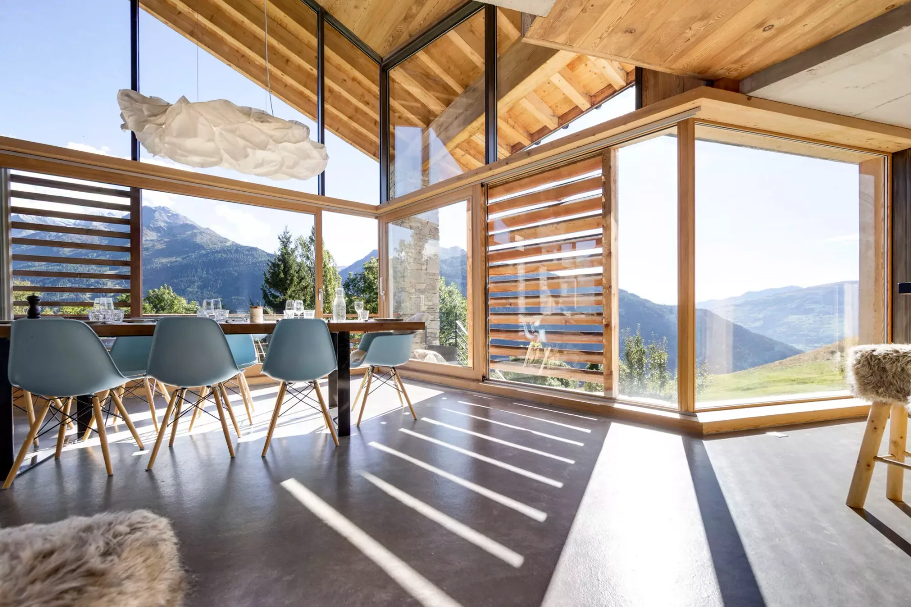 Un comedor luminoso con una mesa y grandes ventanas con vistas a las montañas.