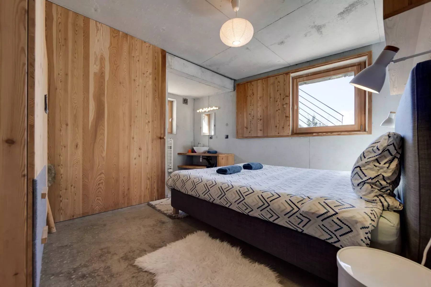 Un dormitorio con una cama, paredes revestidas de madera y una ventana.
