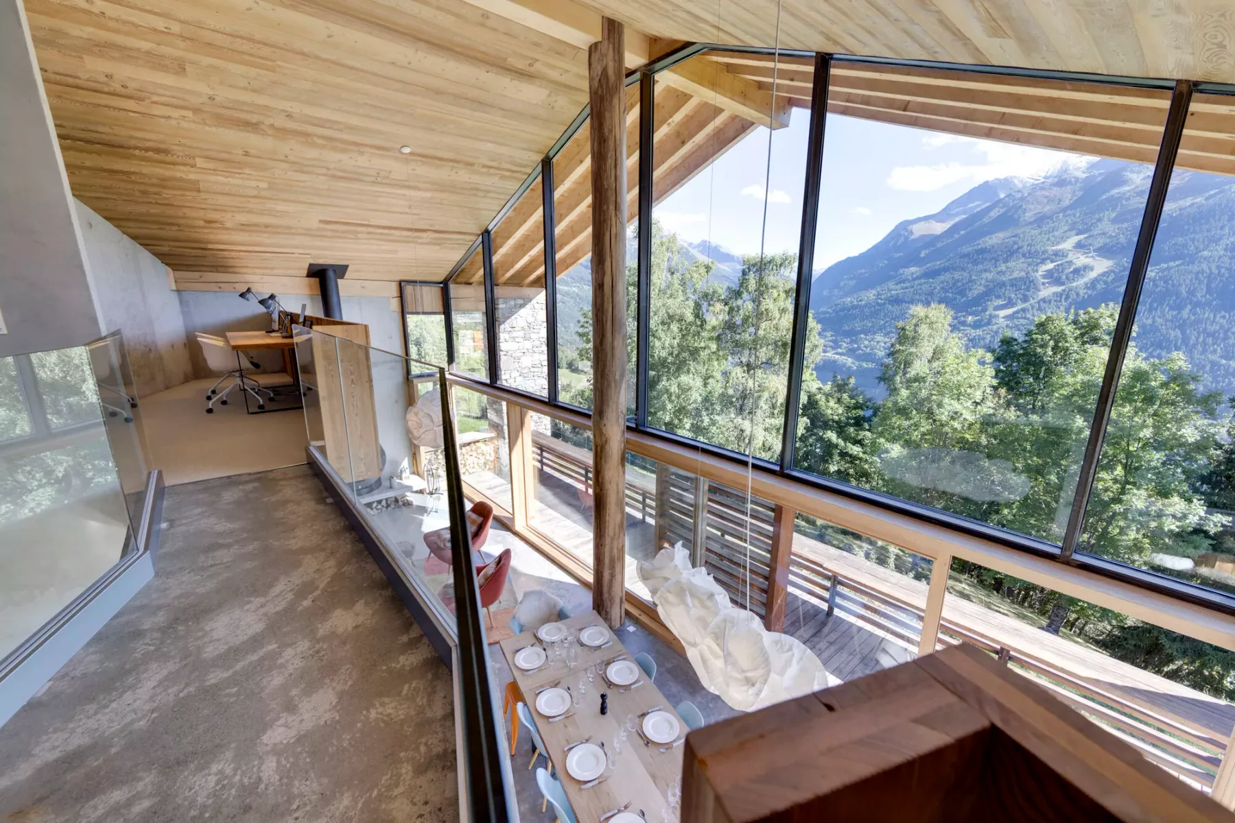 A bright dining area with a long table beside large windows overlooking mountains.