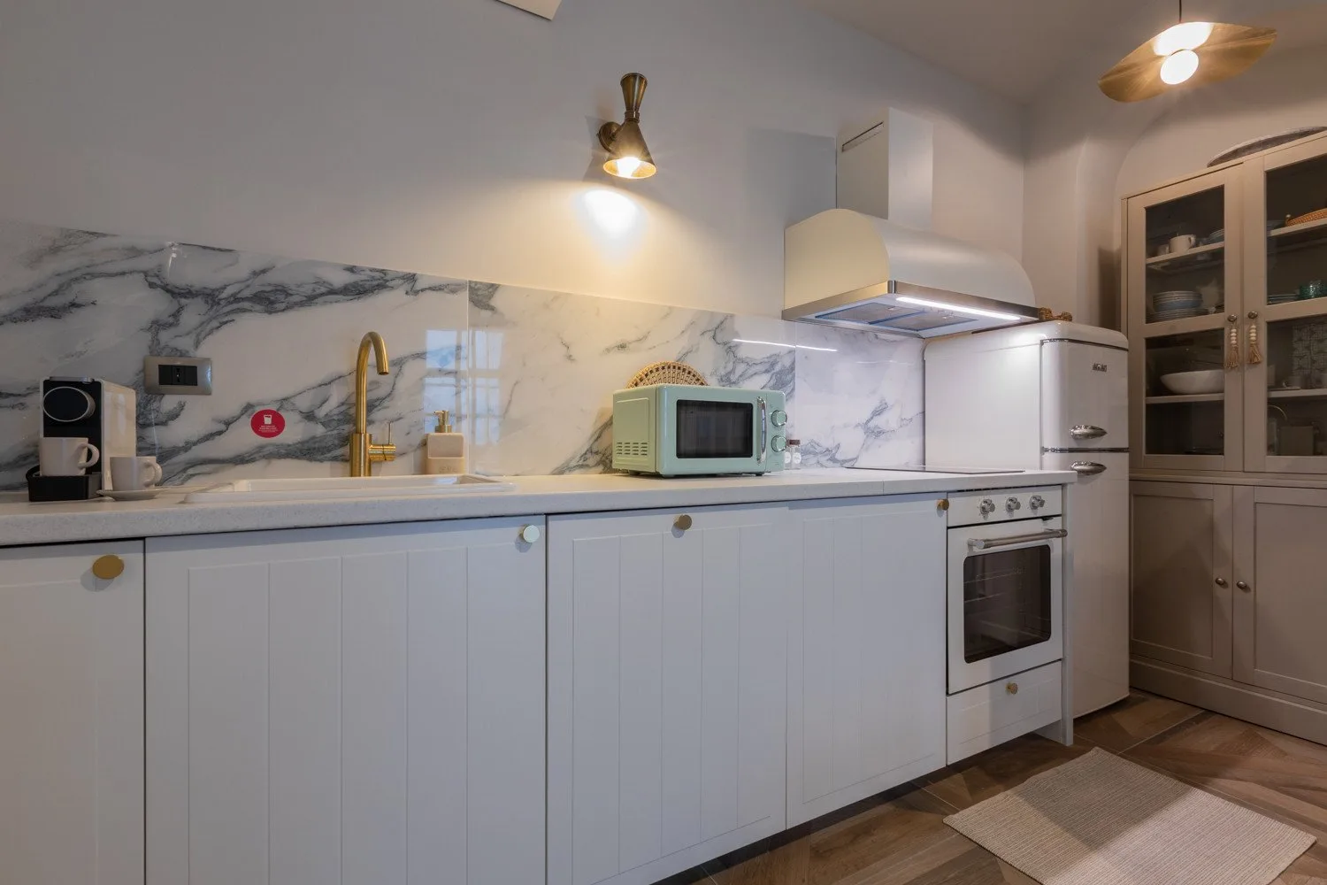 A kitchen with white cabinets and appliances along a marble-patterned backsplash.