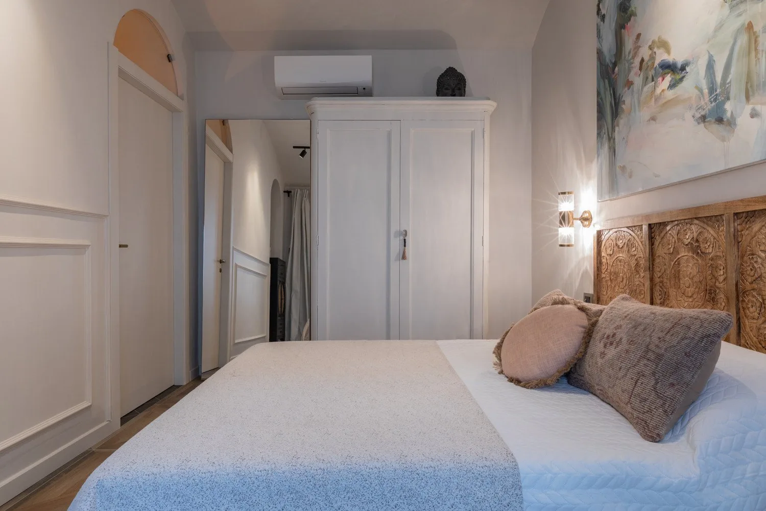 A bedroom with a bed, a white wardrobe, and a large painting above the headboard.