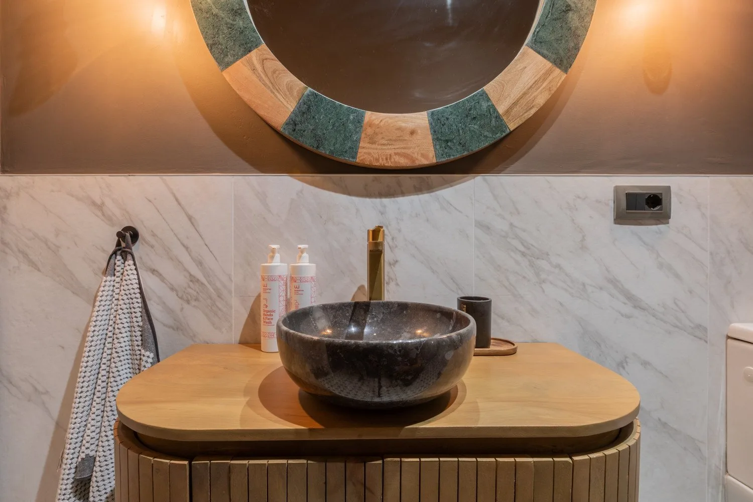 A bathroom vanity with a dark vessel sink and round mirror.