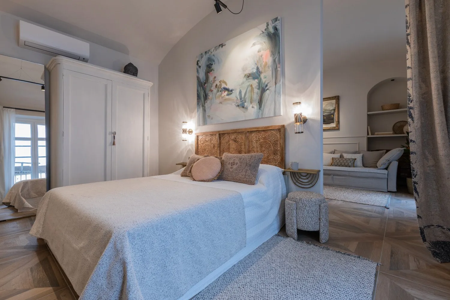 A bedroom with a neatly made bed, wall art, and a wardrobe.