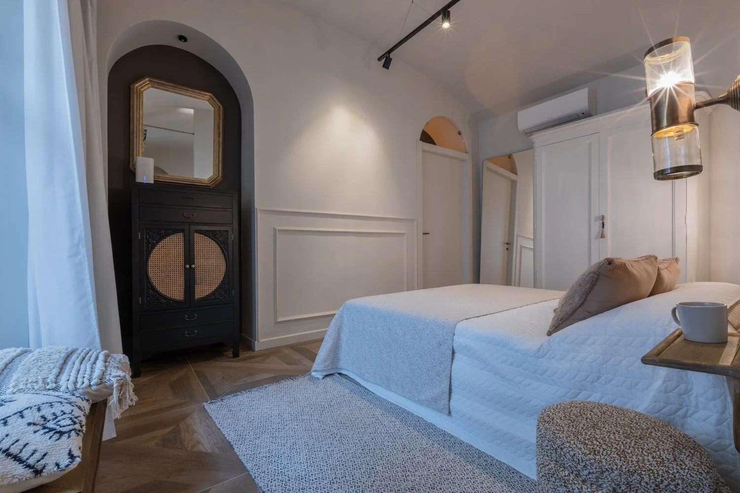 A bedroom with a neatly made bed, a dark cabinet, and soft natural light.