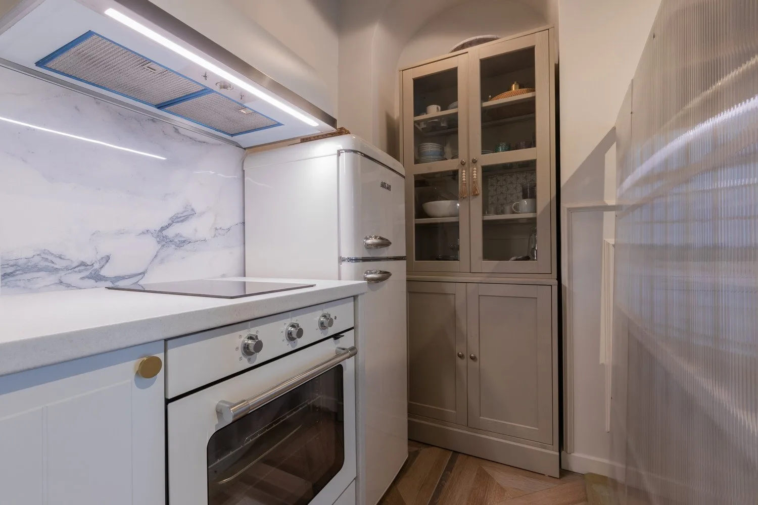 A compact kitchen with a white stove, refrigerator, and glass-front cabinets.