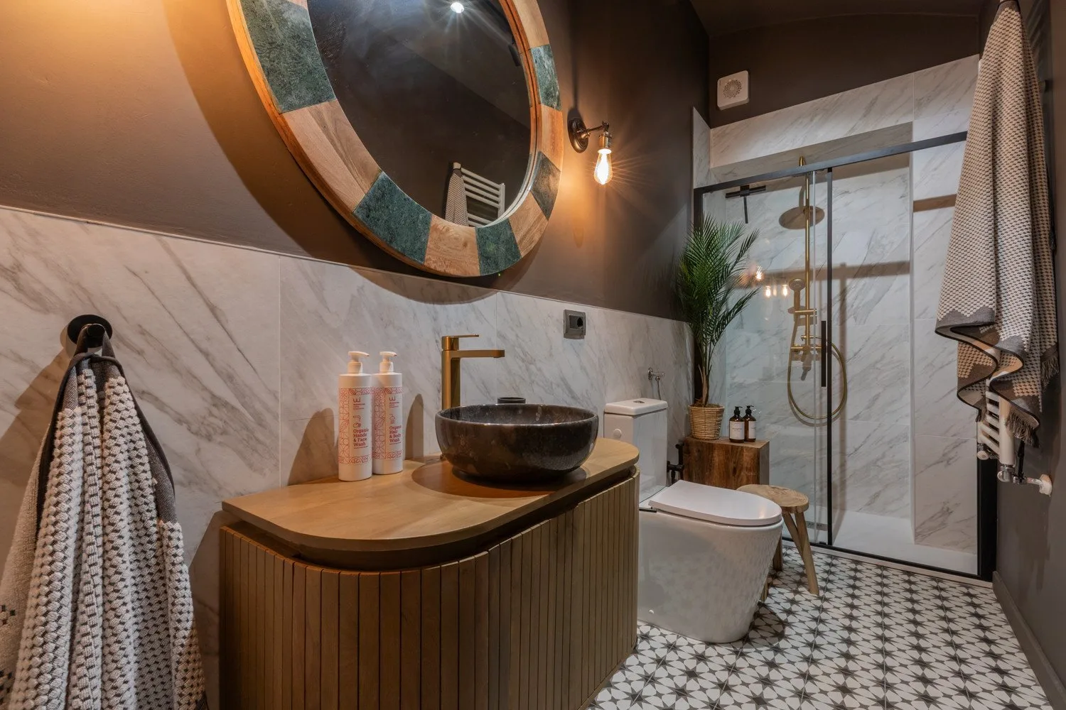 A bathroom with a vessel sink, round mirror, and glass shower area.