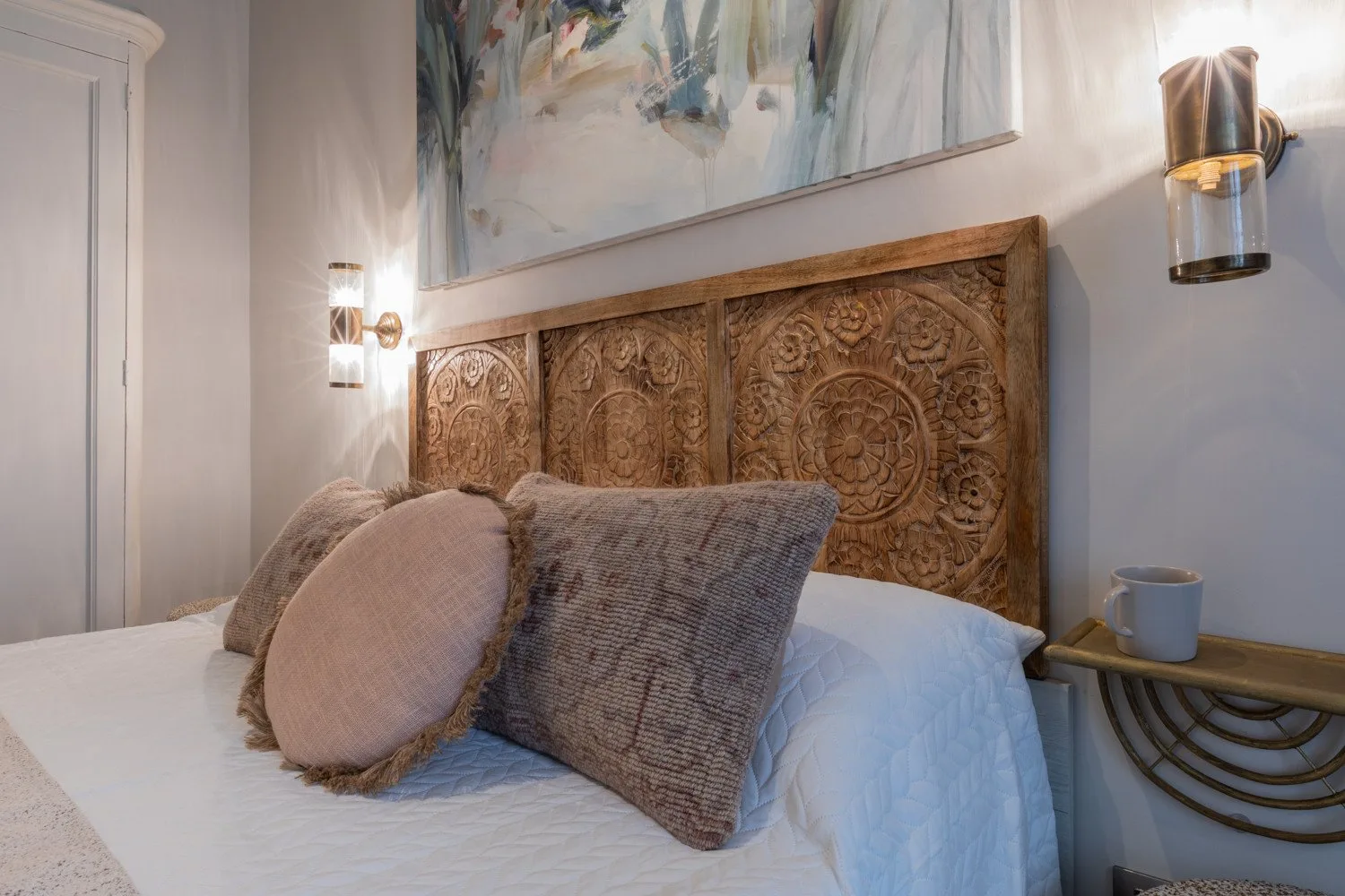 A bedroom with a bed, decorative carved headboard, and wall art.