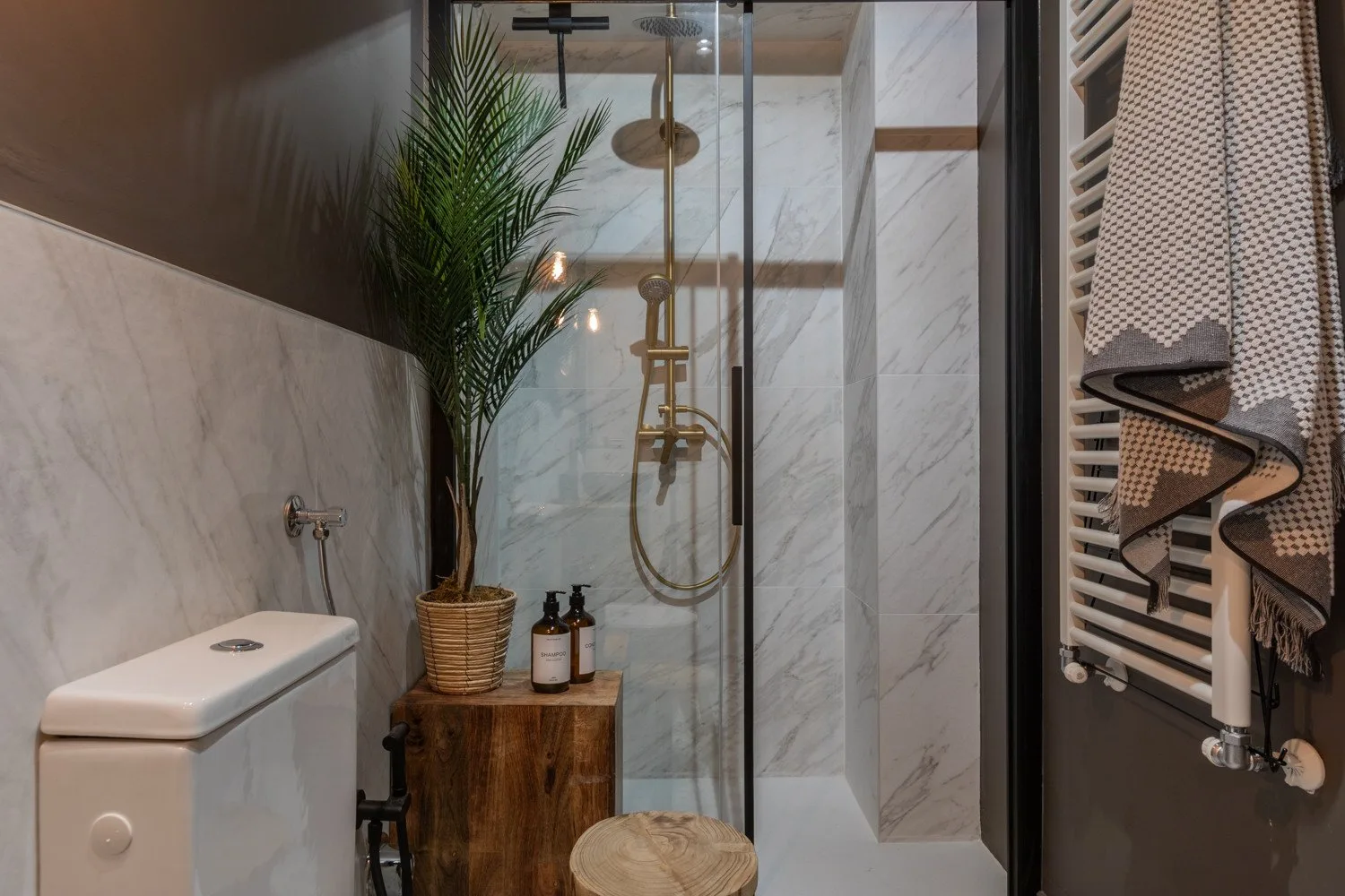 A marble-tiled bathroom with a glass shower and a potted palm.