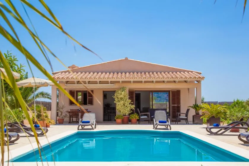 A swimming pool sits in front of a single-story house with a tiled roof.