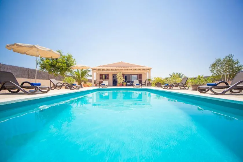 A swimming pool is lined with lounge seating and umbrellas beside a low building.