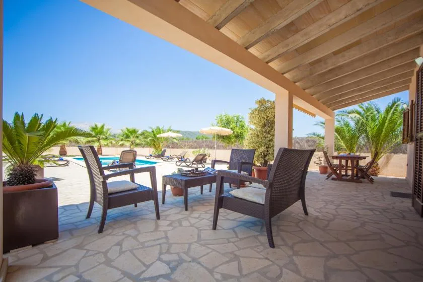 A covered patio with outdoor seating overlooks a sunny pool area.