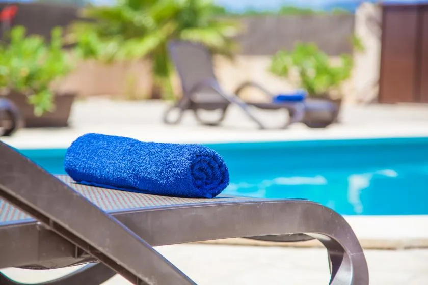 A blue towel rests on a lounge chair beside a swimming pool.