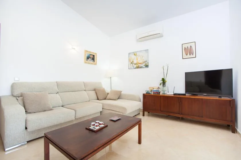 A bright living room with light seating, a coffee table, and a television.