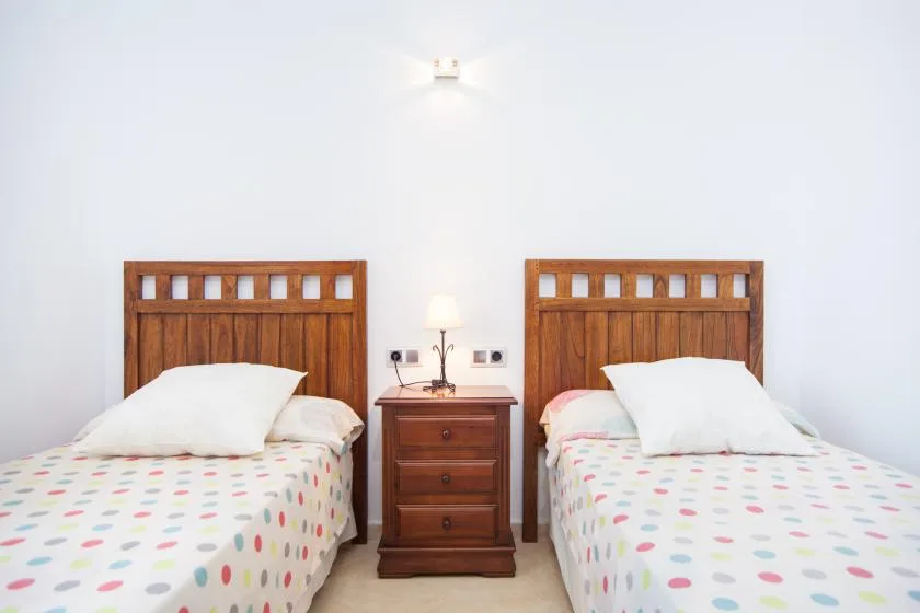 A bedroom with two beds and a wooden bedside table between them.