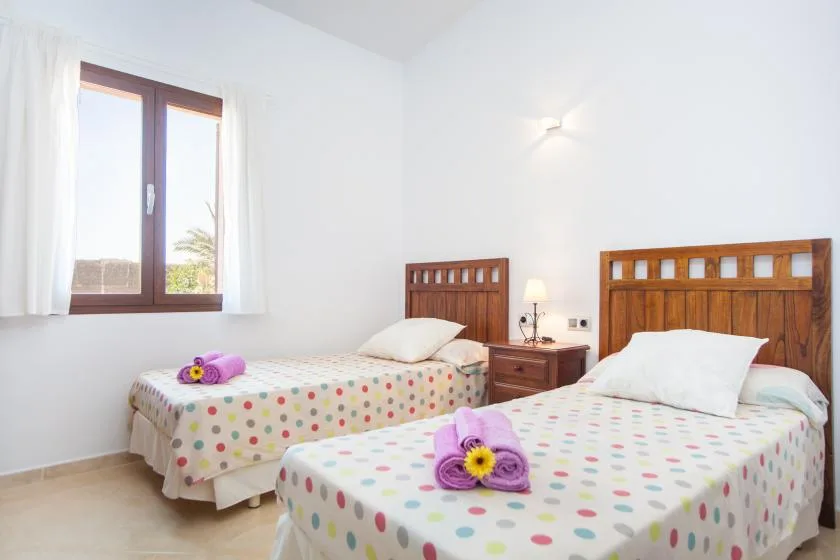 A bright bedroom with two beds, colorful bedding, and a window.