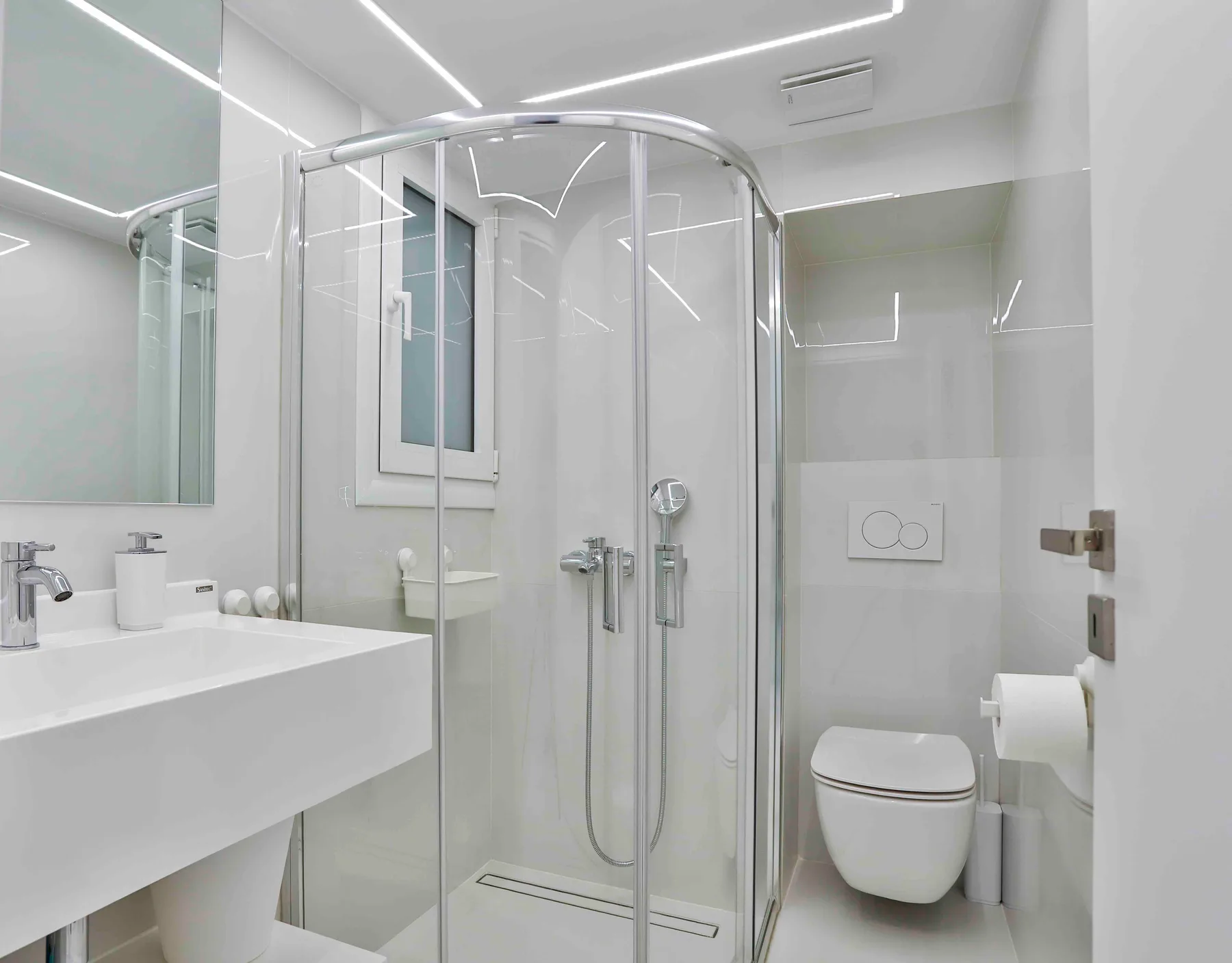 Baño luminoso con ducha de vidrio y lavabo suspendido.