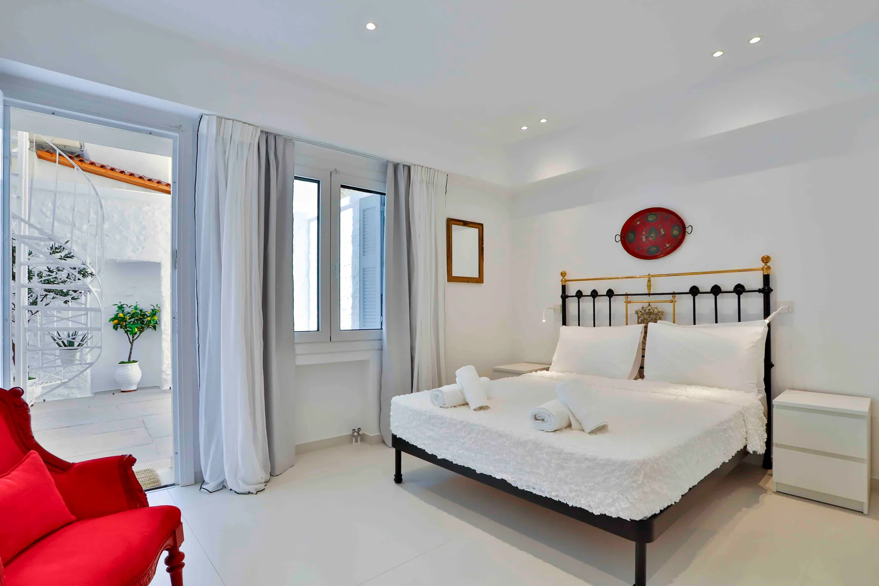 Un dormitorio luminoso con cama, mesita de noche y ventanas que dan a un balcón.