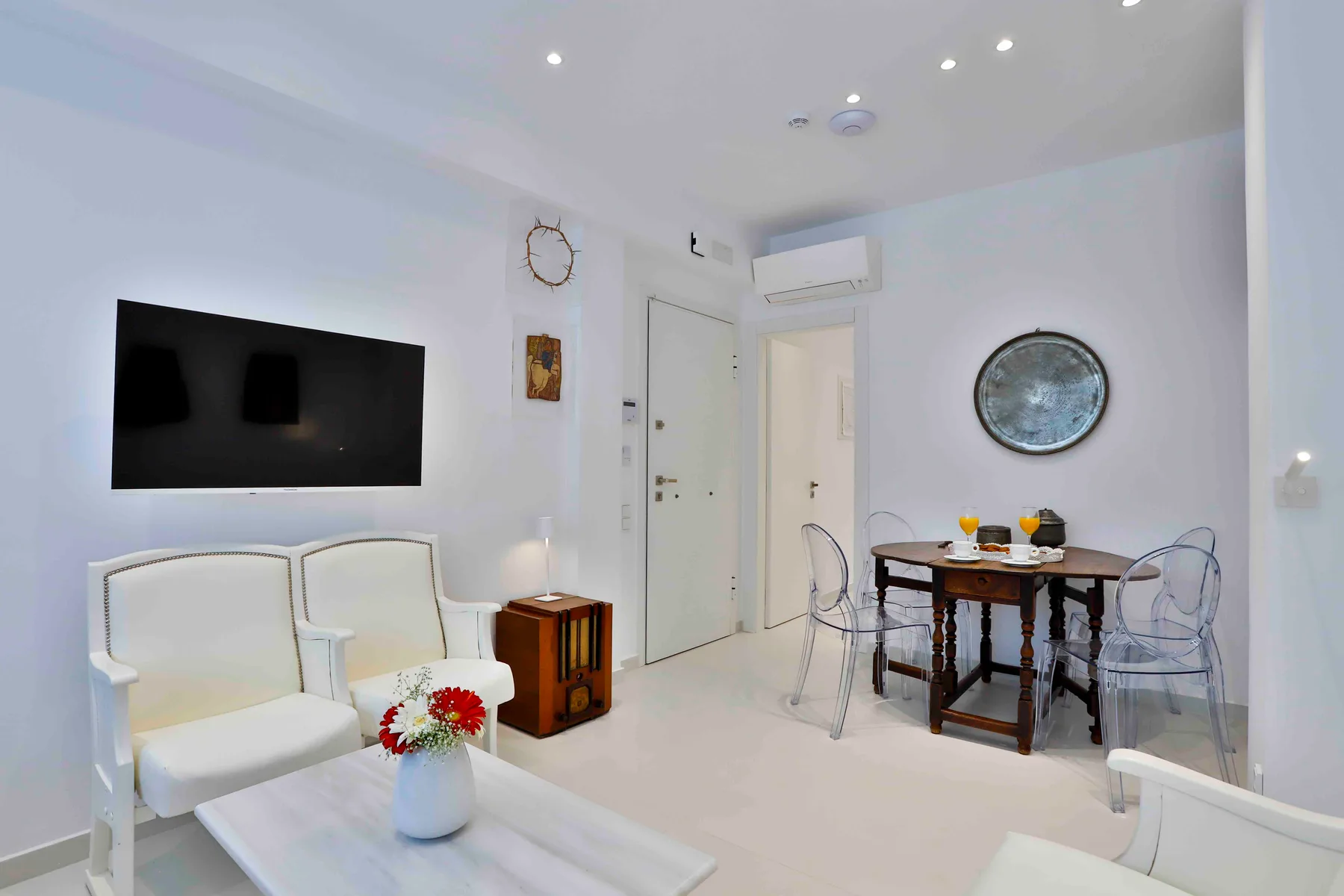 Una luminosa sala de estar con asientos, un televisor en la pared y una pequeña mesa de comedor.
