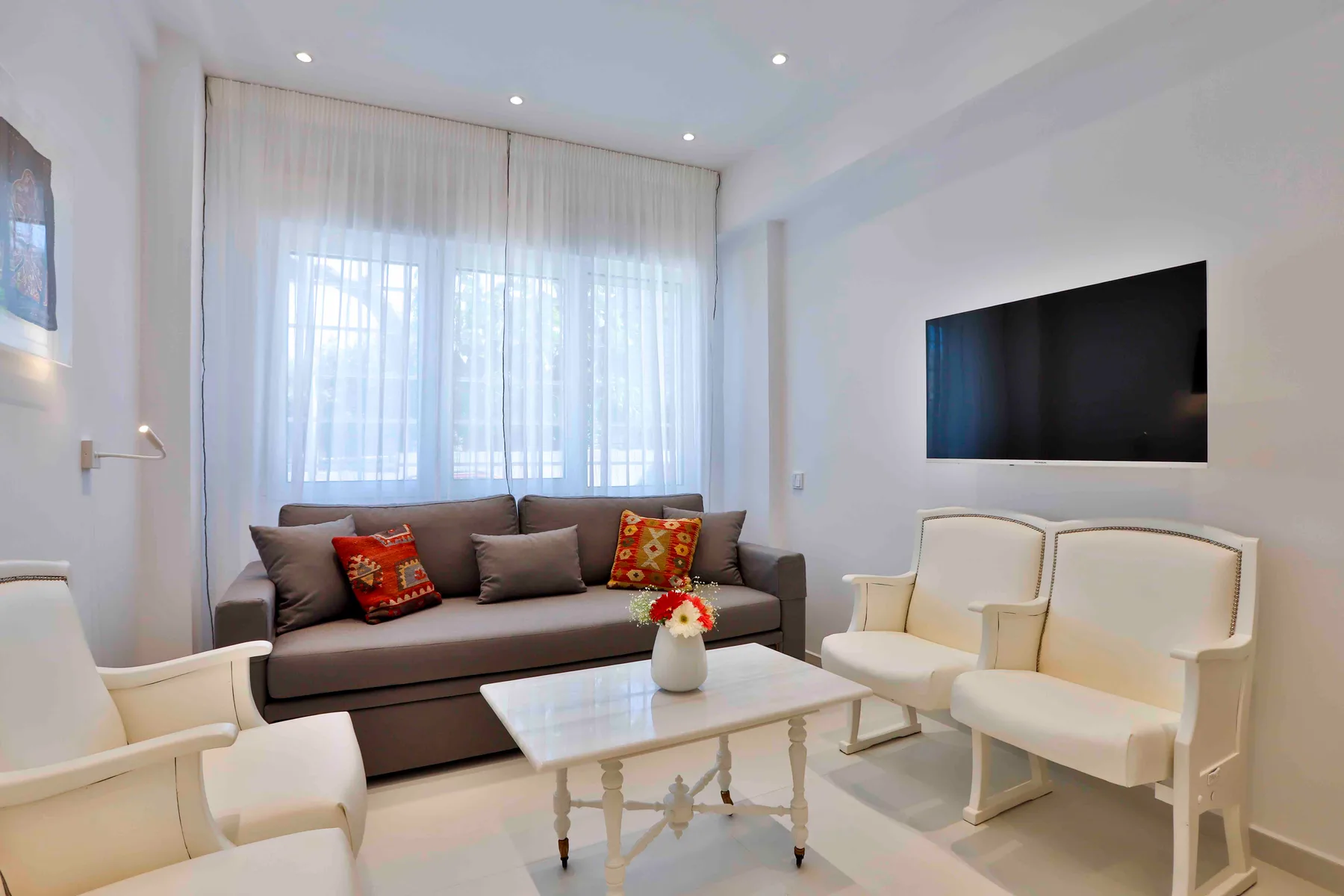 Una sala luminosa con asientos alrededor de una mesa de centro y un televisor en la pared.
