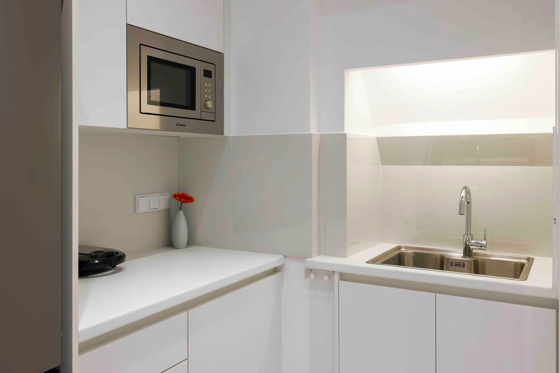 Una cocina compacta con encimeras blancas, un fregadero y un microondas integrado.