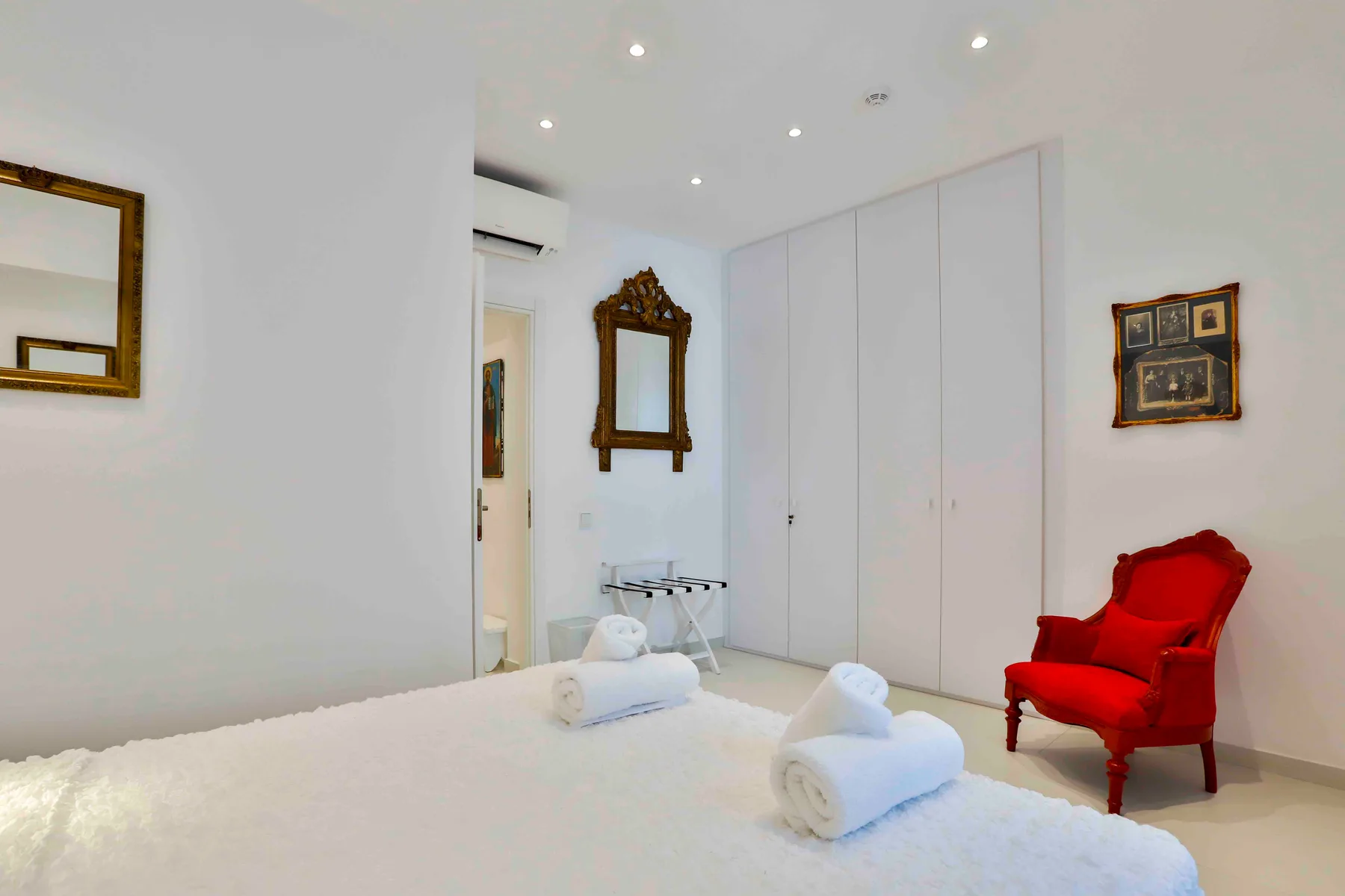 Un dormitorio luminoso con un sillón rojo y toallas sobre la cama.
