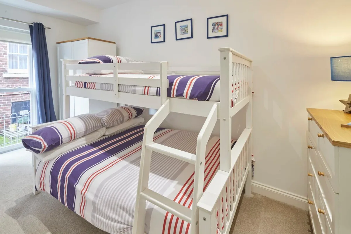 A bedroom with white bunk beds dressed in striped bedding.
