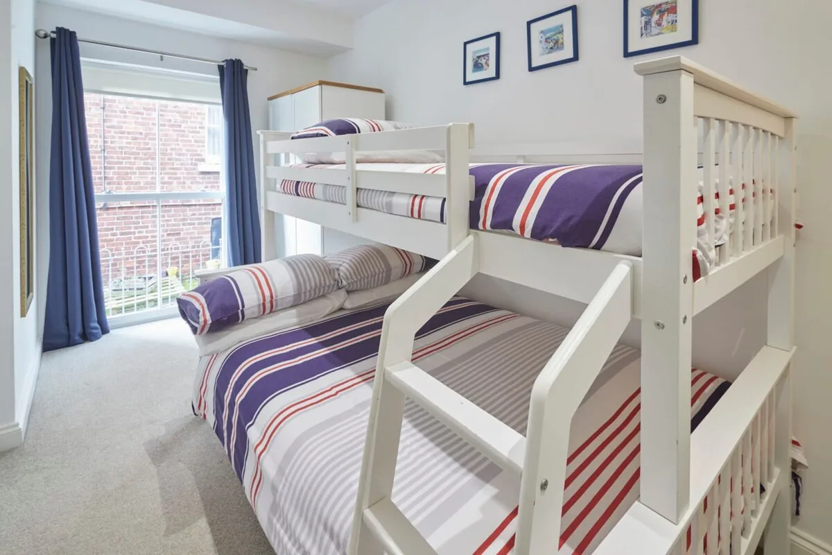 A bedroom with white bunk beds dressed in striped bedding.