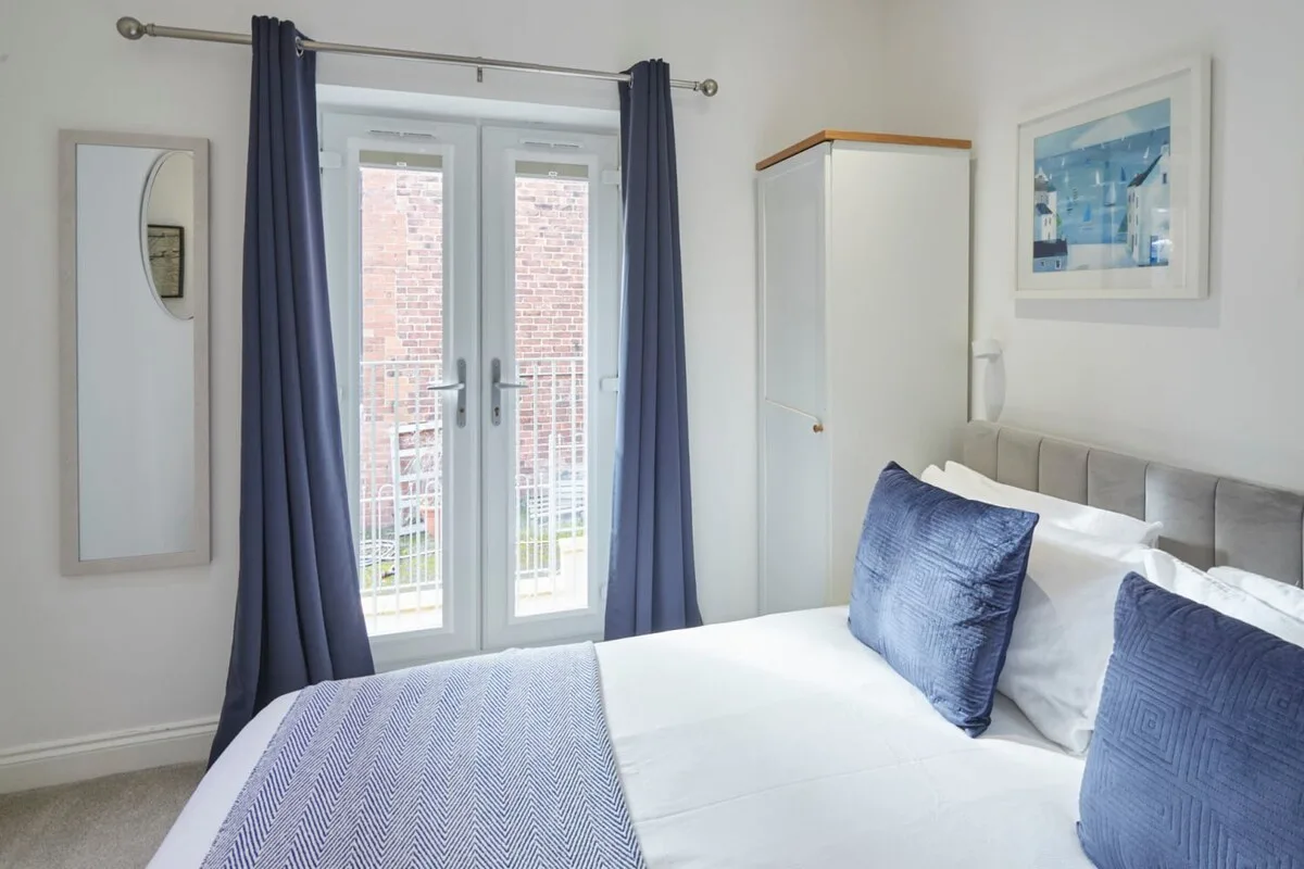 A bedroom with a neatly made bed and blue curtains beside the window.