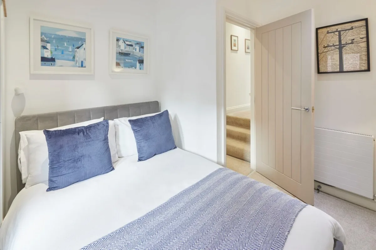 A bedroom with a neatly made bed and a doorway leading to a hallway.