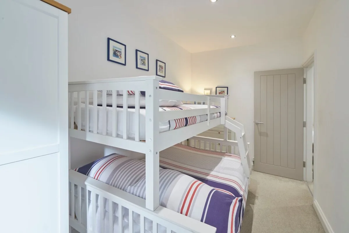 A bright bedroom with white bunk beds and striped bedding.