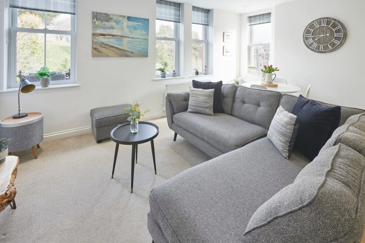 A bright living room with gray seating, large windows, and a small coffee table.