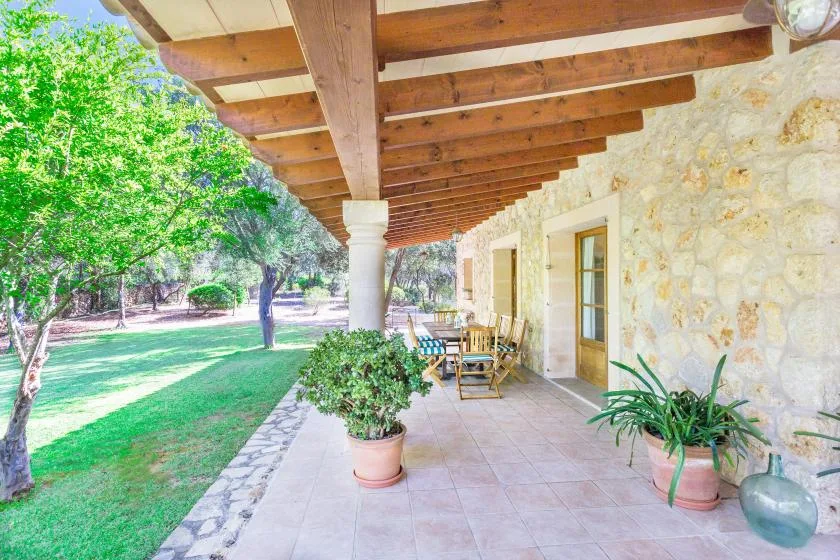 A covered outdoor patio with seating and potted plants beside a stone wall.