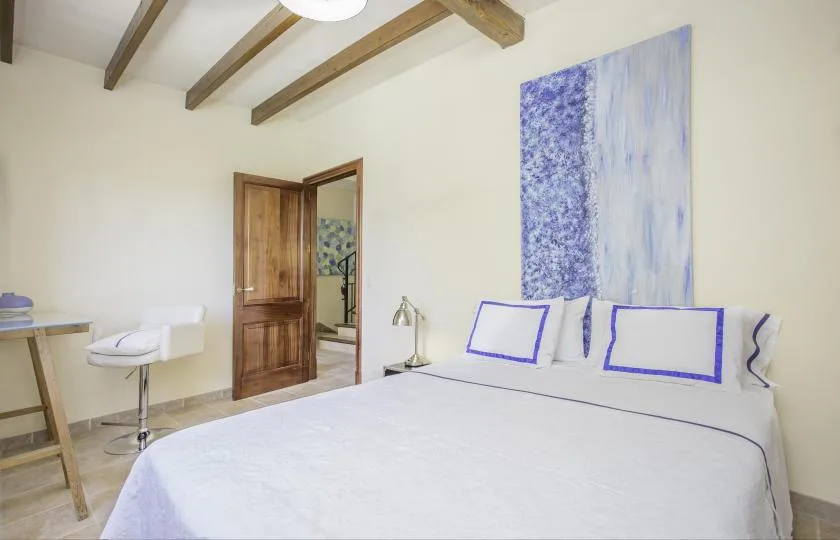 A bedroom with a large bed, blue-accented pillows, and exposed ceiling beams.