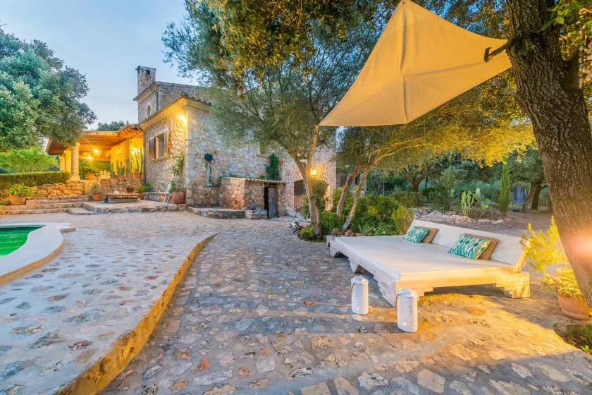 A stone-paved outdoor patio with a low lounge seating area beneath a shade sail.