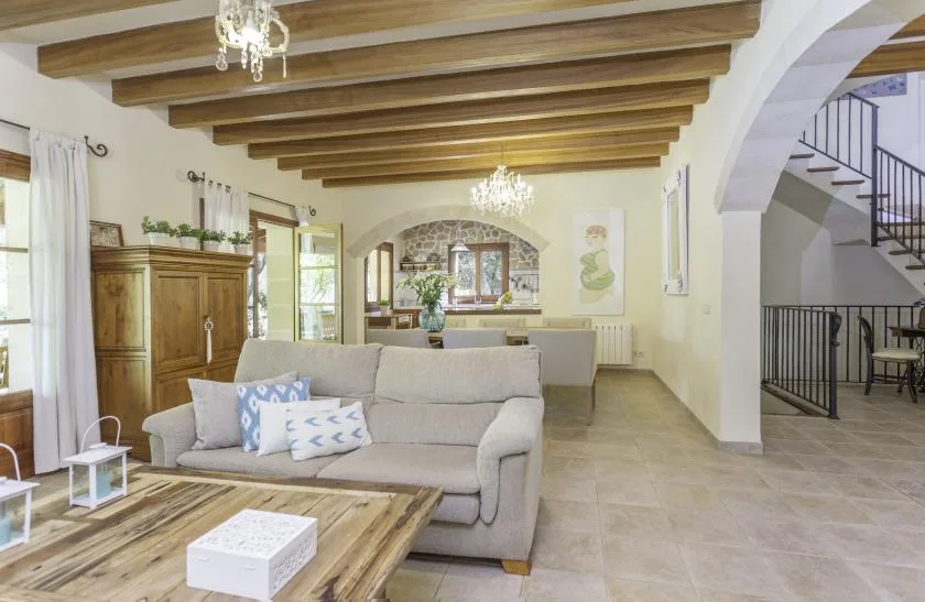 A bright living room with a sofa, wooden ceiling beams, and a dining area beyond.