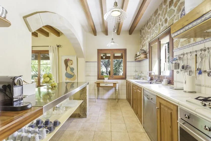 A bright kitchen with wooden cabinets, stone walls, and a central worktable.
