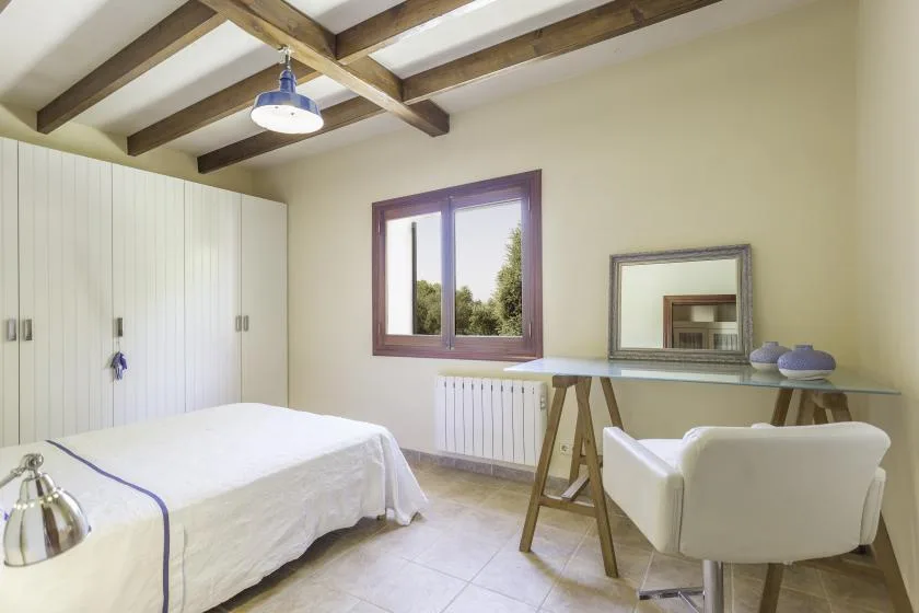A bedroom with a bed, a wardrobe, and a desk beneath exposed ceiling beams.