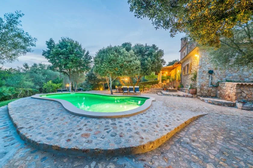 An outdoor swimming pool sits beside a stone building and paved courtyard.