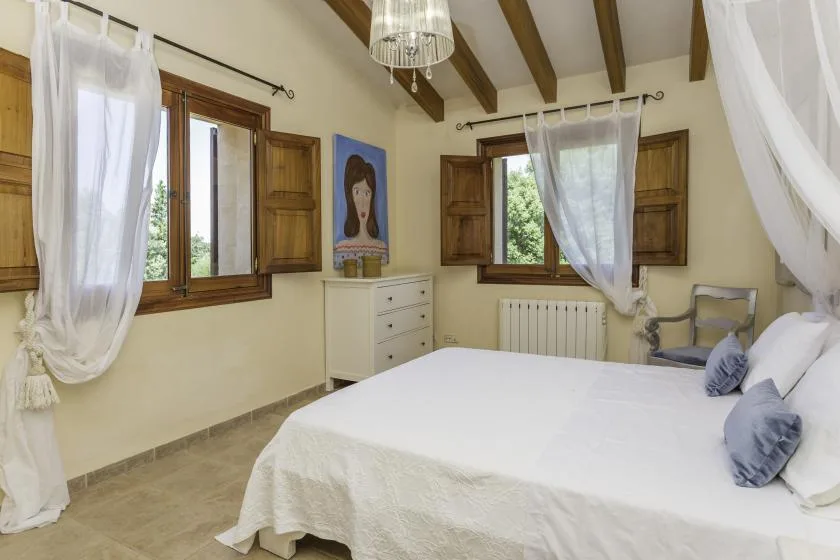 A bedroom with a large bed, wooden windows, and sheer curtains.