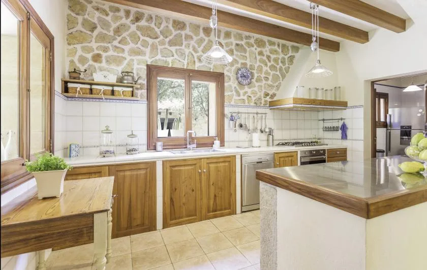 A spacious kitchen with wooden cabinets, stone walls, and a central island.