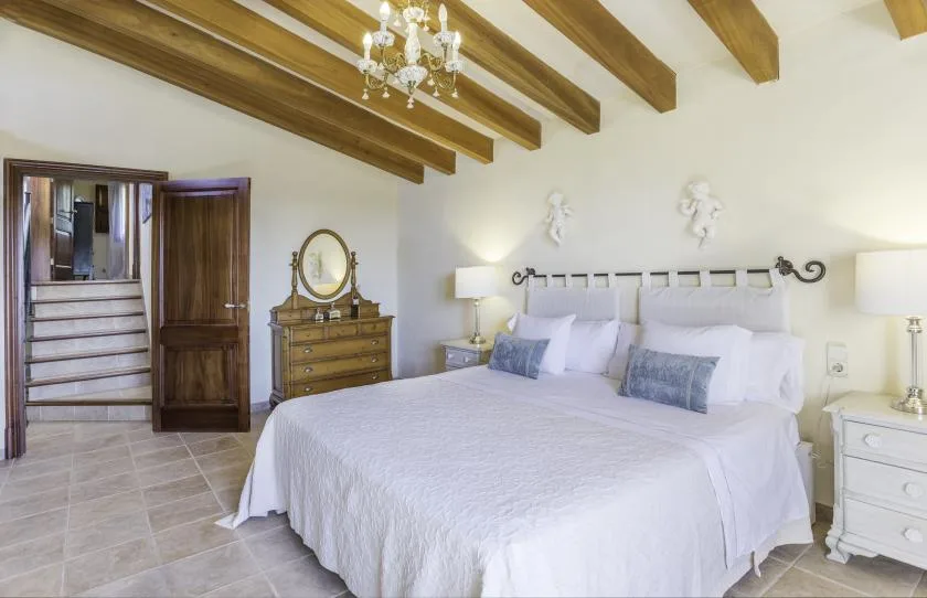 A bedroom with a large bed, bedside tables, and exposed ceiling beams.